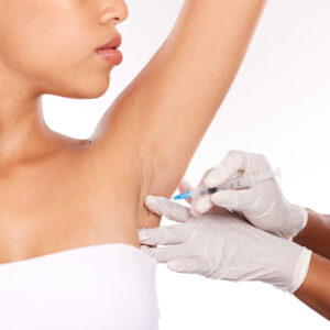 Frau lässt sich mit erhobenem Arm durch eine Injektion die Achsel unterspritzen